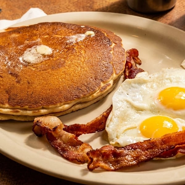 A breakfast plate with a stack of pancakes, two fried eggs, and crispy bacon strips.