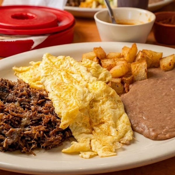 A breakfast plate with shredded beef, scrambled eggs, home fries, and refried beans.