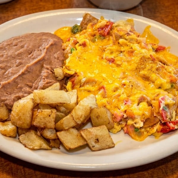 A breakfast plate with cheesy scrambled eggs, refried beans, home fries, and a tortilla.
